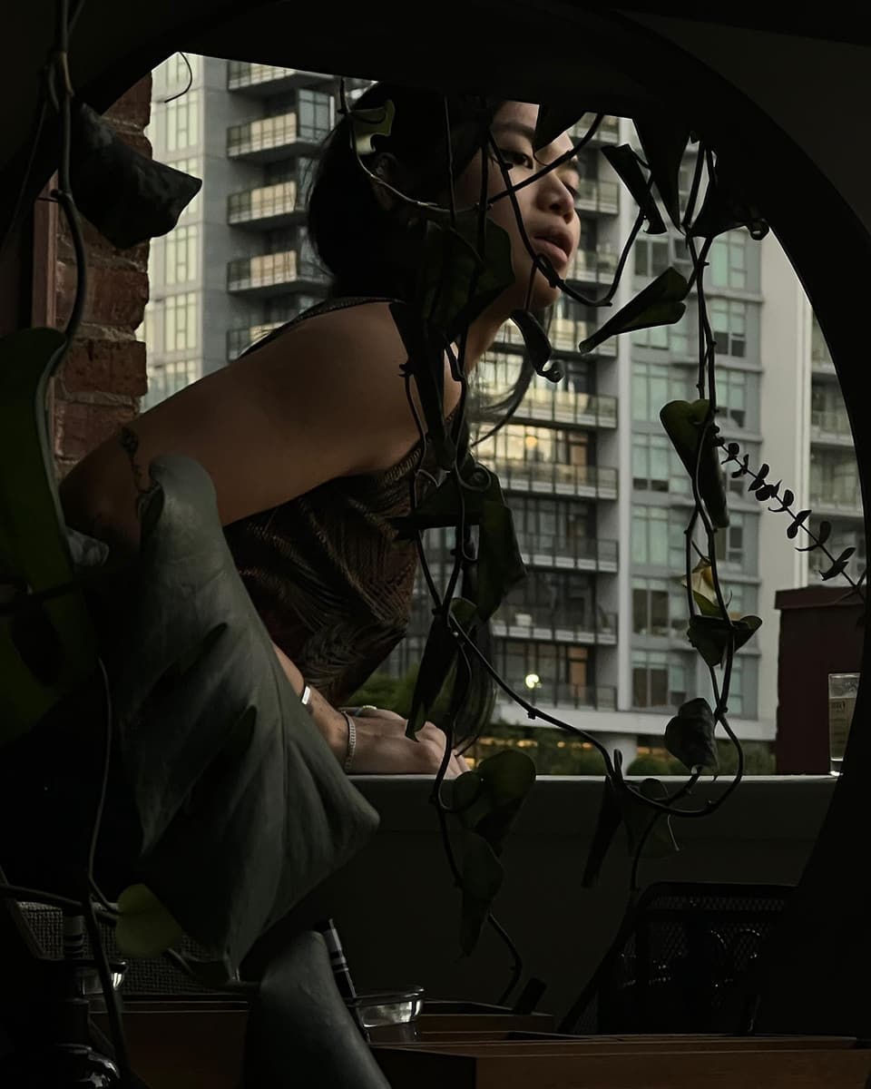 sel on a balcony at golden hour, vines all around, the city behind